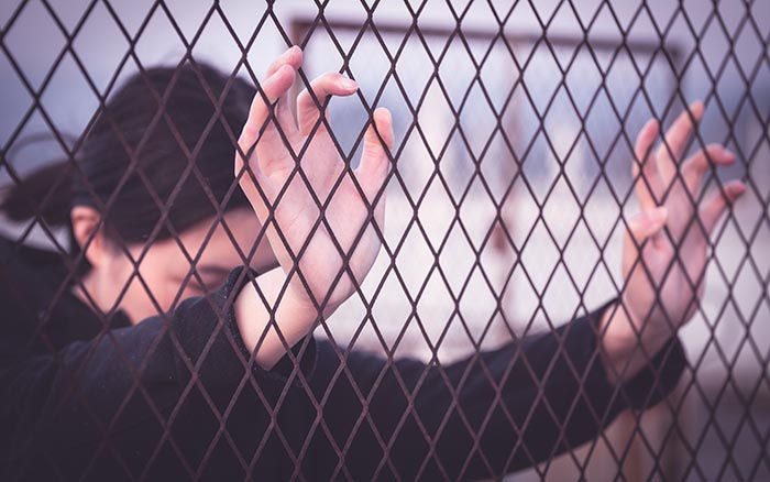 woman with hands against chain link fence