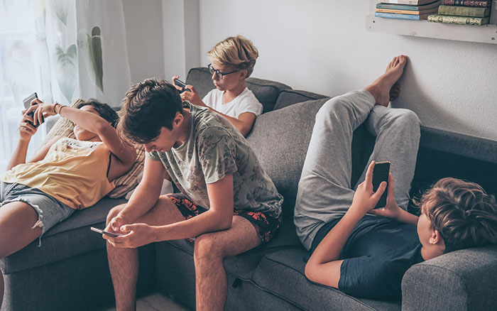 4 teens using smartphones on a couch