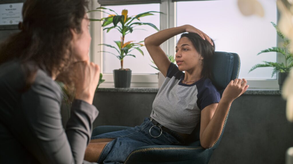 Relaxed African American teen girl sits in chair, talks and shares positive emotions with psychologist on counseling therapy session. Female therapist provides psychotherapy for teenager. Psychology.